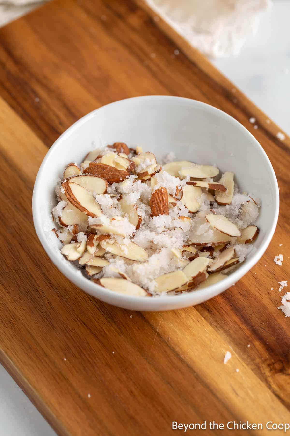 Sliced almonds and sugar mixed together in a small white bowl. 