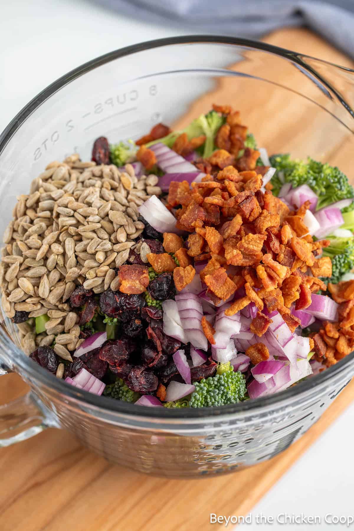 A glass bowl filled with broccoli, bacon, sunflower seeds and dried cranberries.