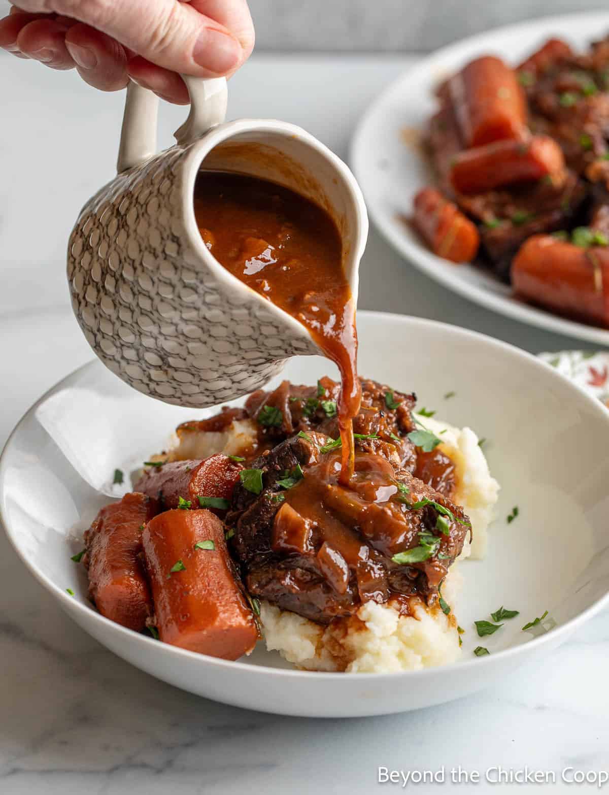 Sauce being poured over pot roast and potatoes. 