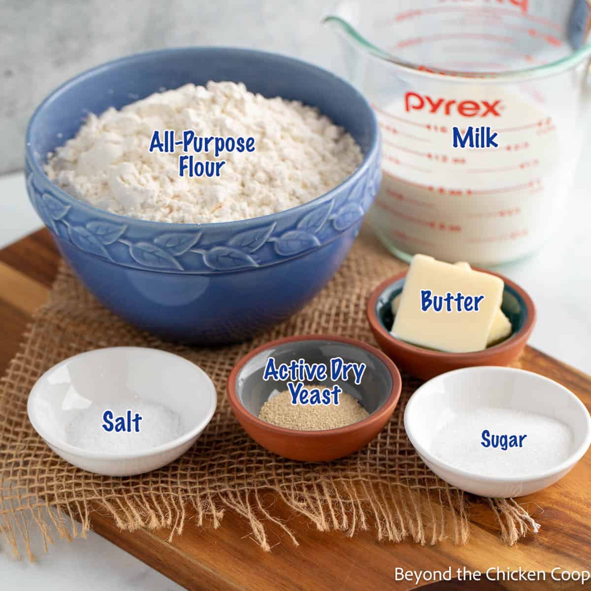 Small bowls filled with yeast, sugar, butter, salt and flour. 