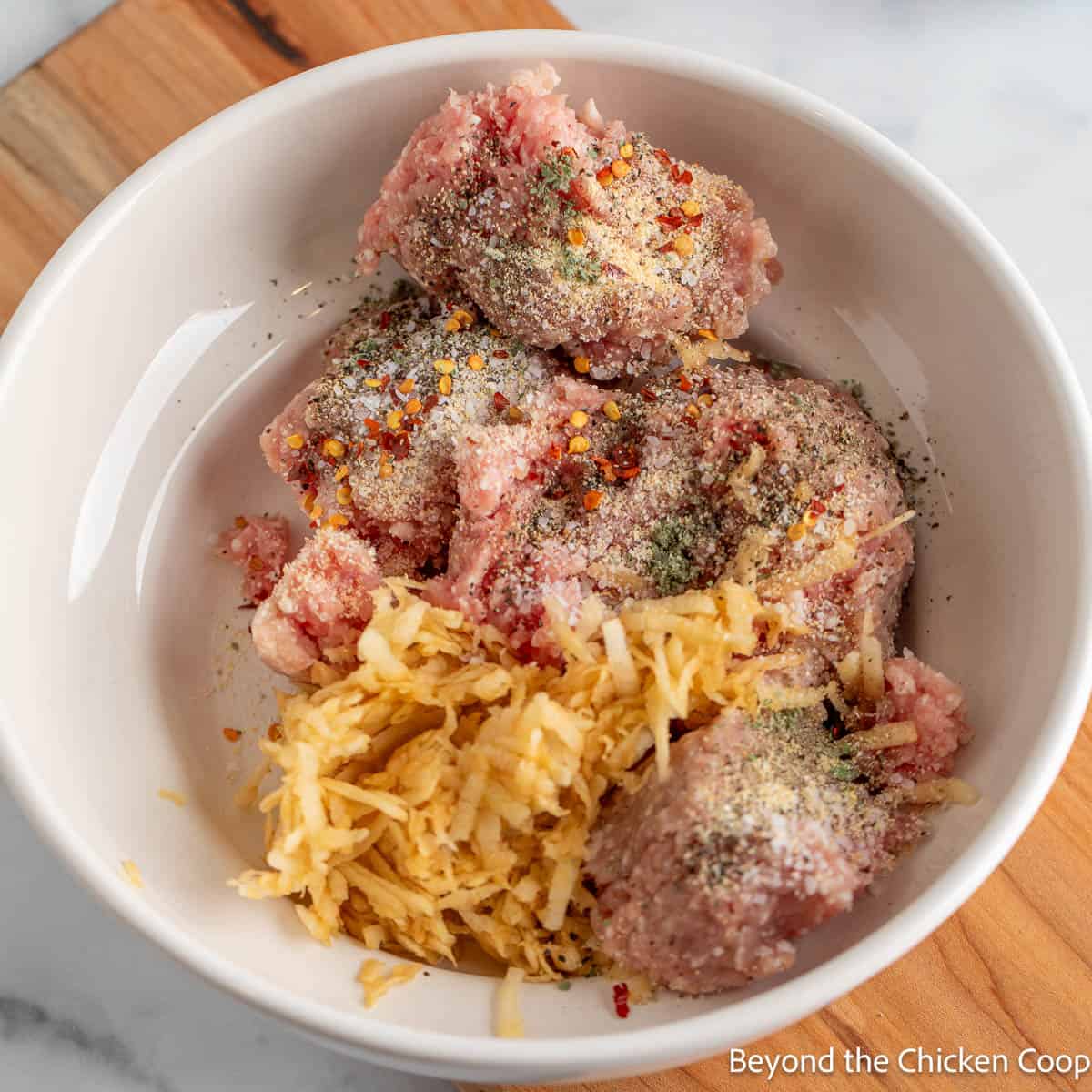 Ground pork, grated apples, and seasoning in a white bowl.