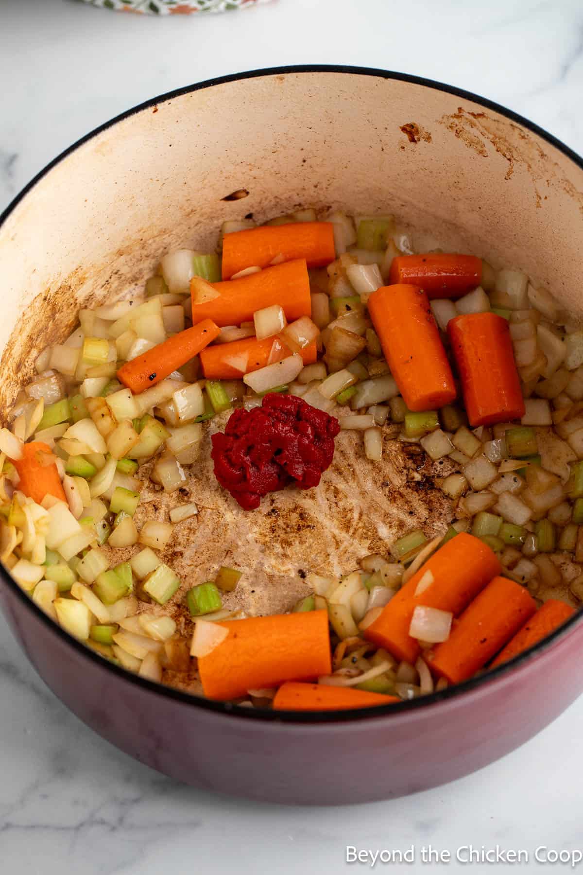 Tomato paste added to the center of a pot with veggies. 