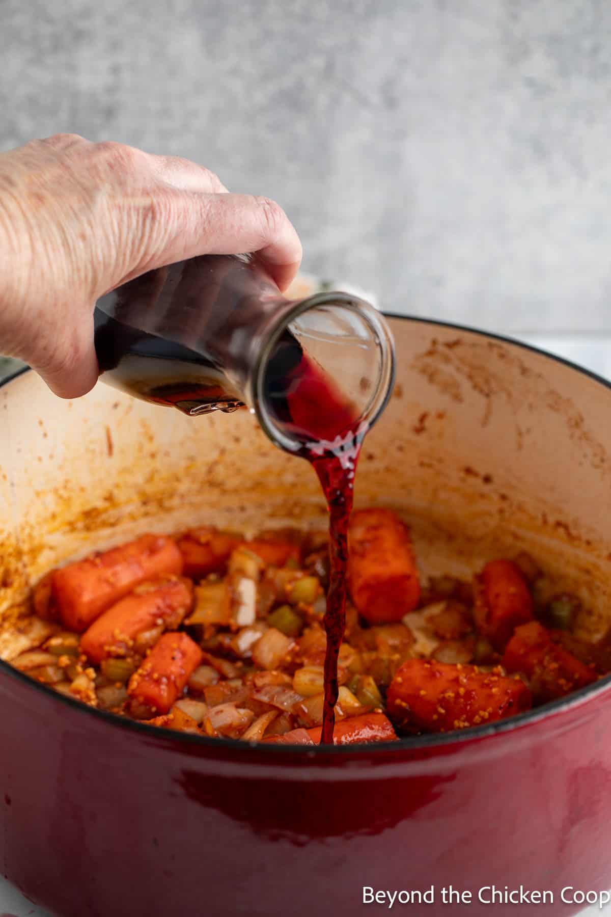 Adding red wine to a pot to deglaze the pan. 