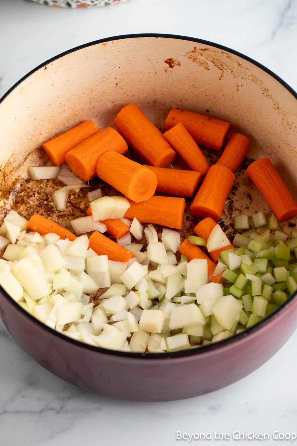 Sauteing carrots, celery, and onions in a red dutch oven pot. 