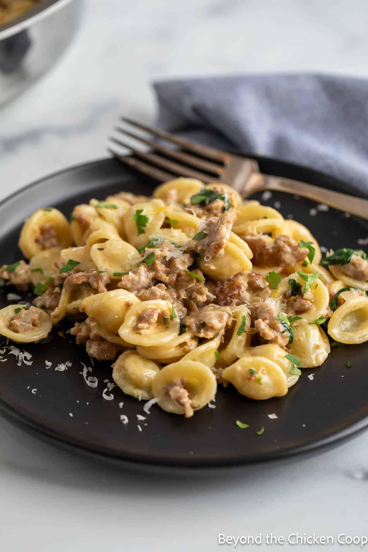 Orecchiette pasta with Italian sausage and spinach on a black plate. 