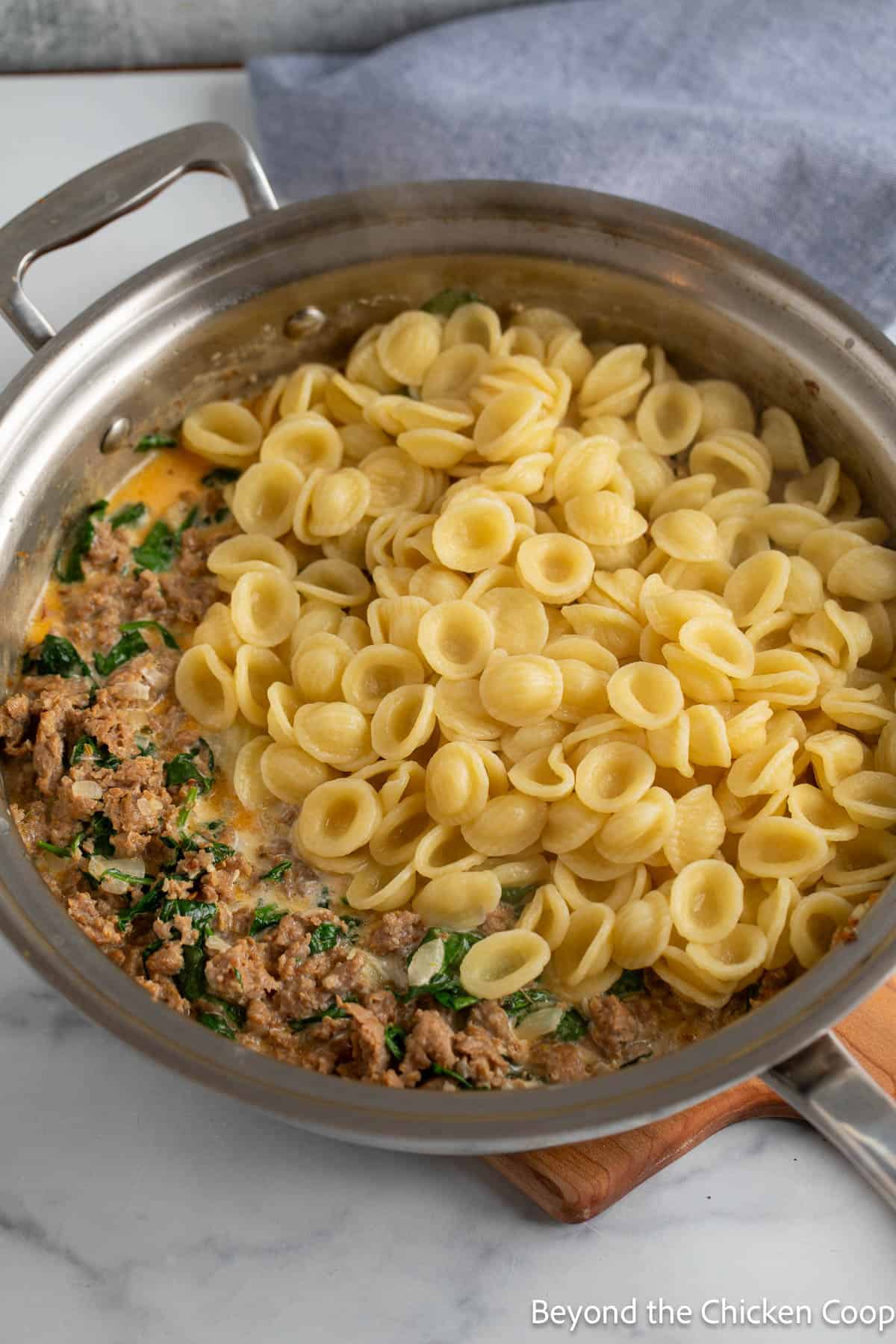 Pasta added to a skillet with cooked sausage. 