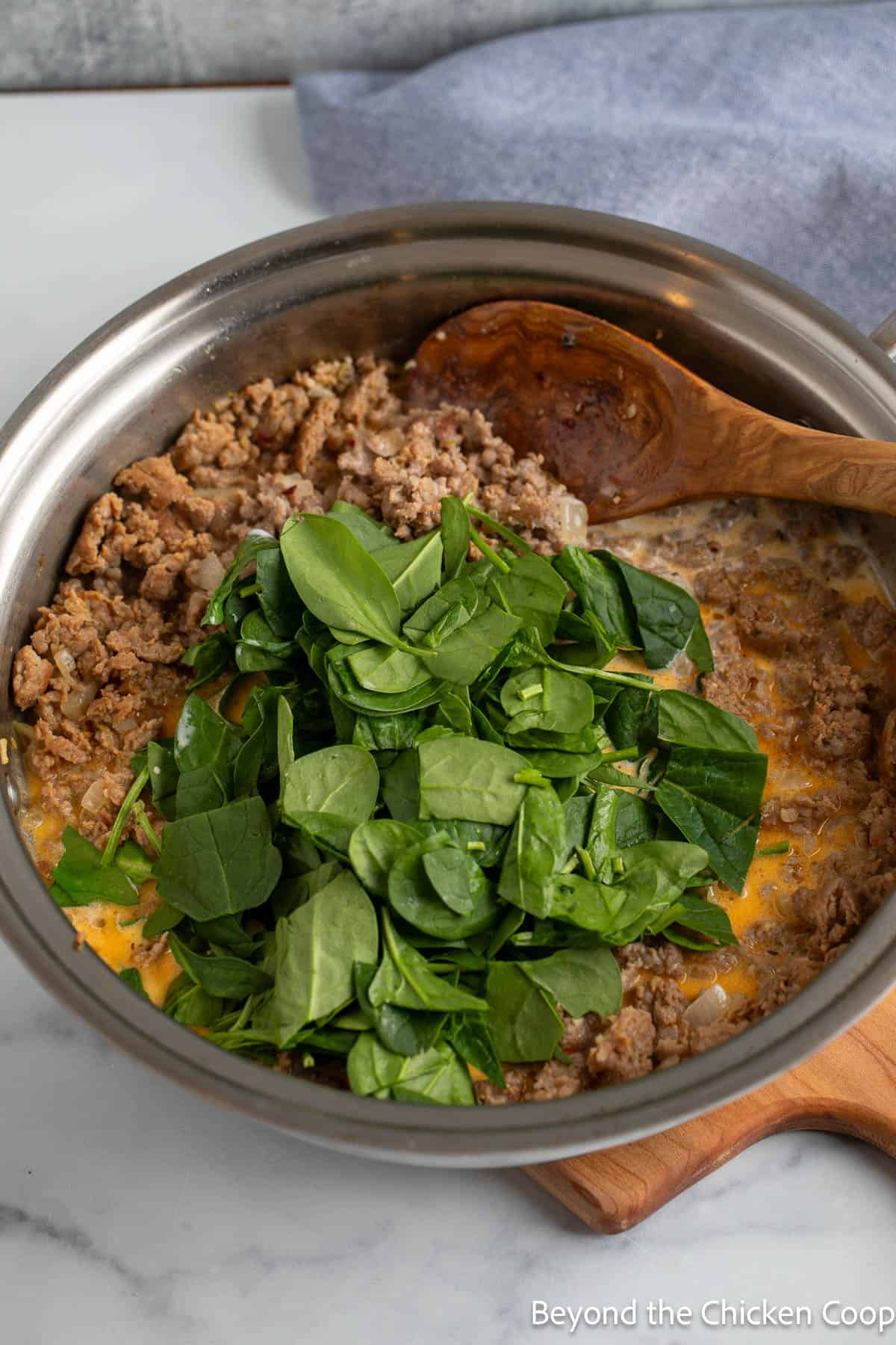 Spinach added to a large skillet with meat. 