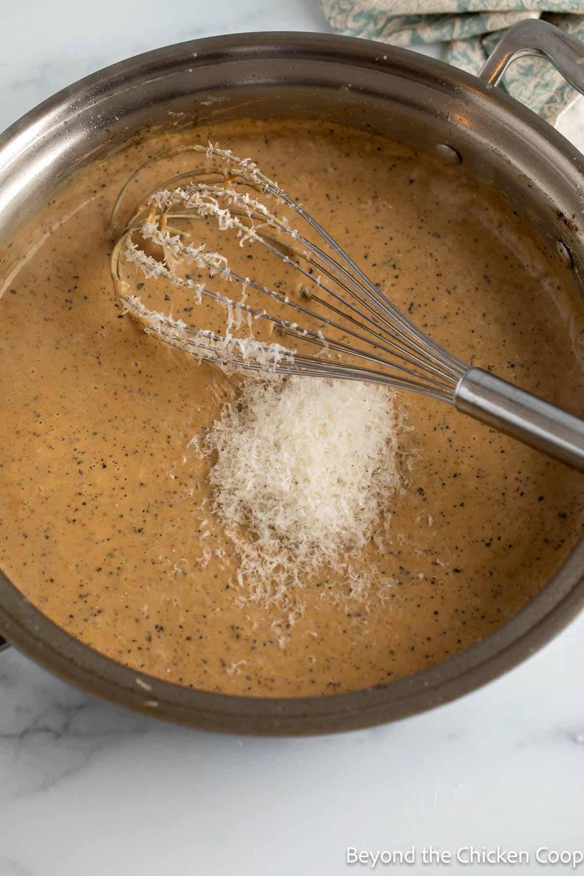 Alfredo sauce in a pan with Parmesan cheese on top. 