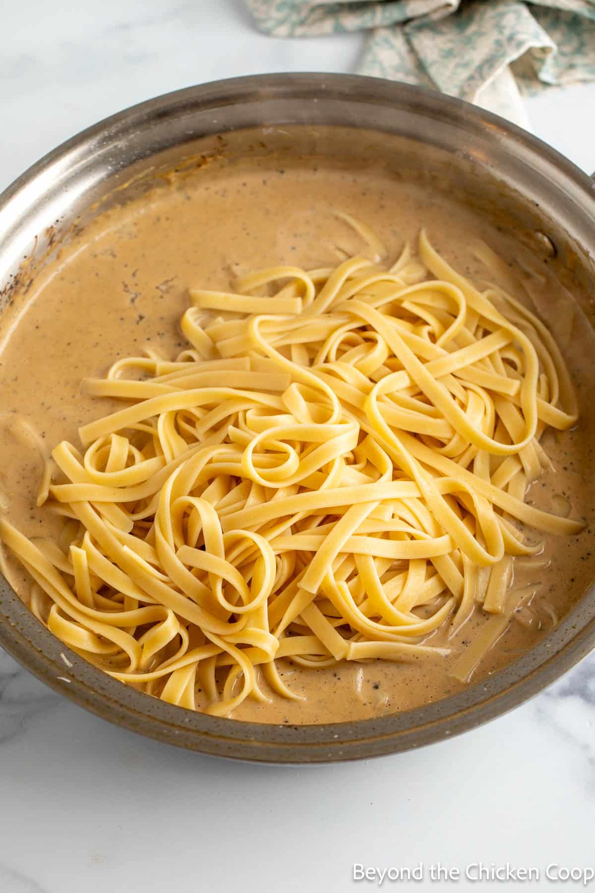 Fettuccine pasta in a pan with Alfredo sauce.