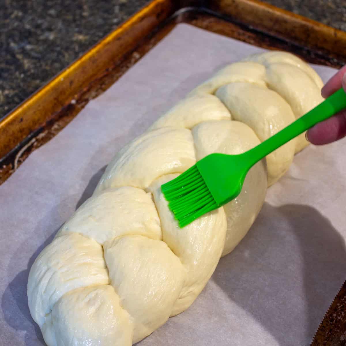 Brushing egg white on a braided loaf of bread.