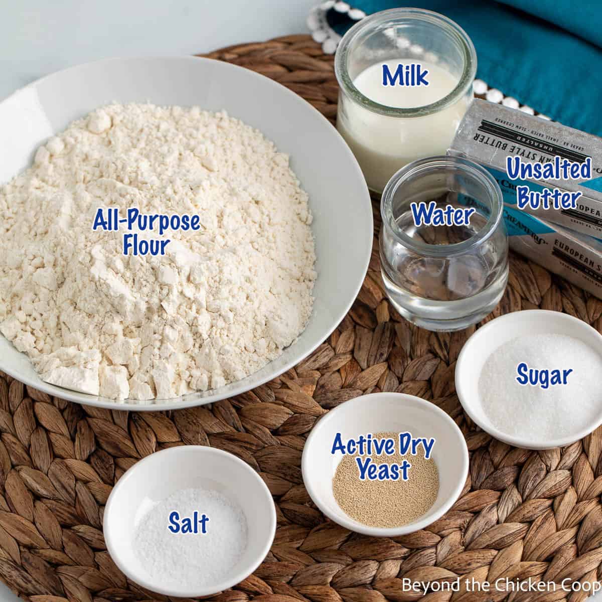 A bowl of flour next to small bowls with salt, sugar, and yeast. 