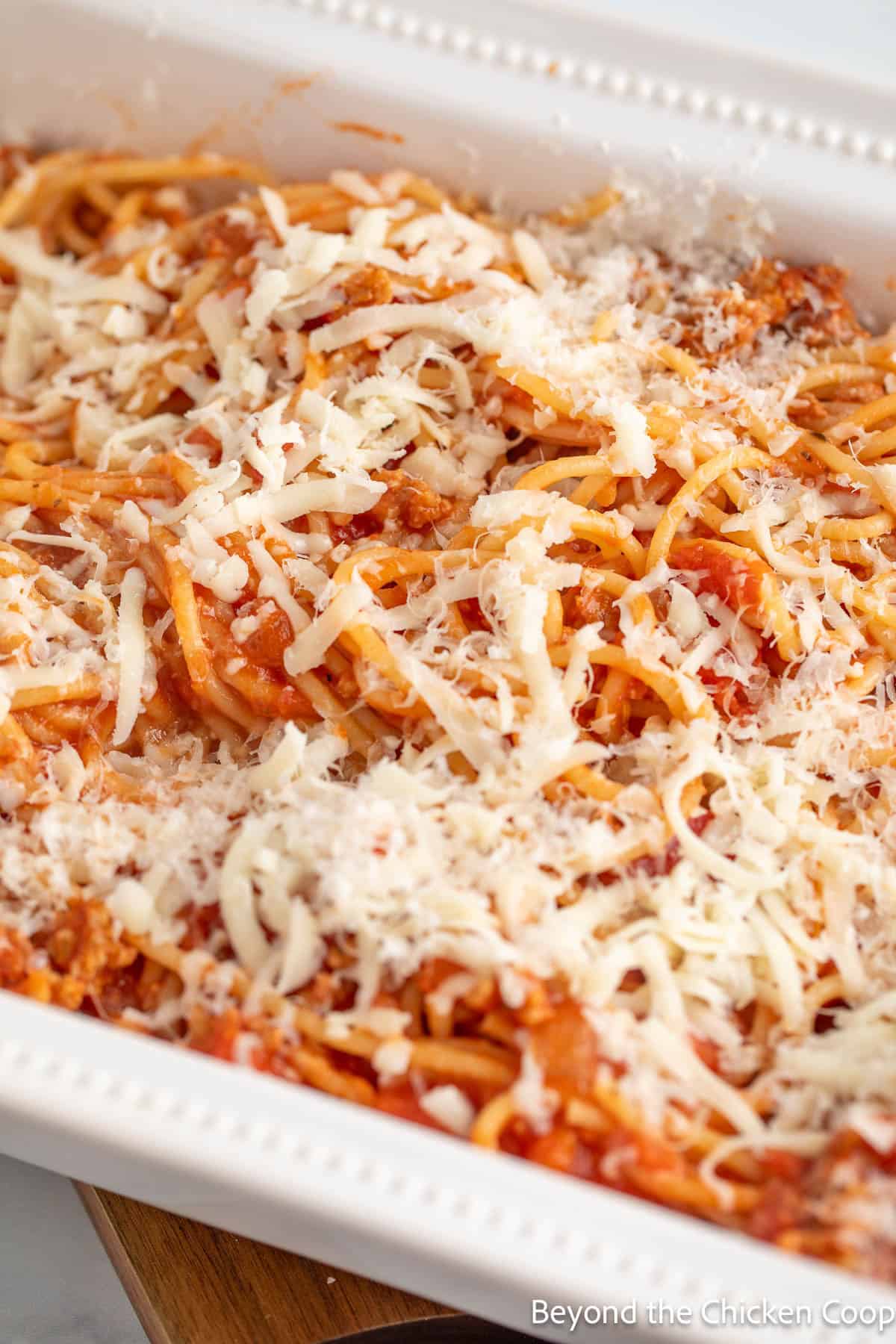 Spaghetti with sauce topped with cheese in a casserole dish.