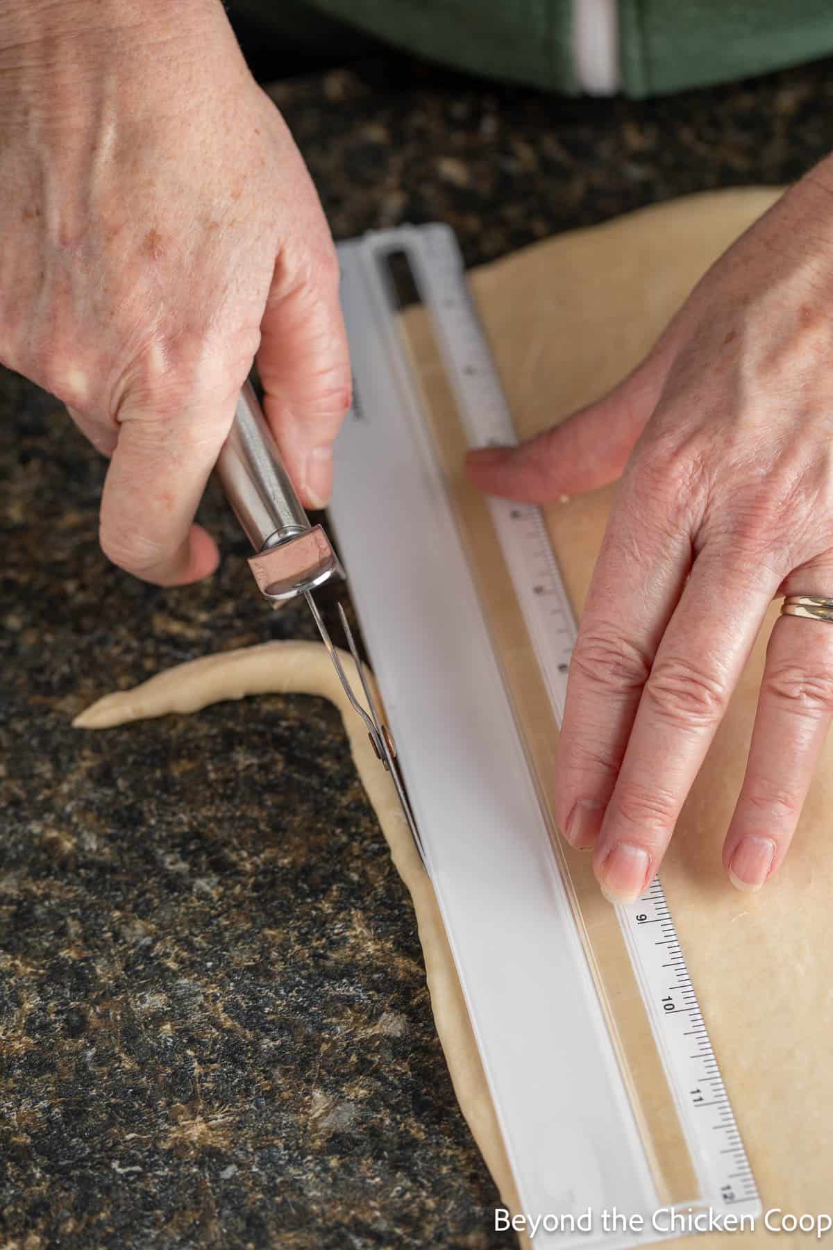 Trimming croissant dough with a pizza cutter and a ruler. 