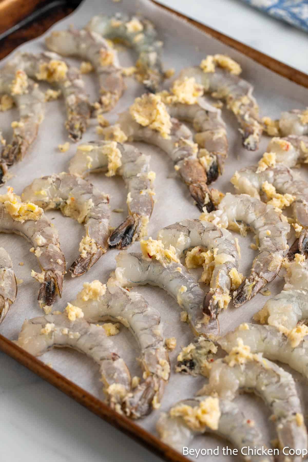 Raw shrimp covered in garlic butter on a sheet pan. 