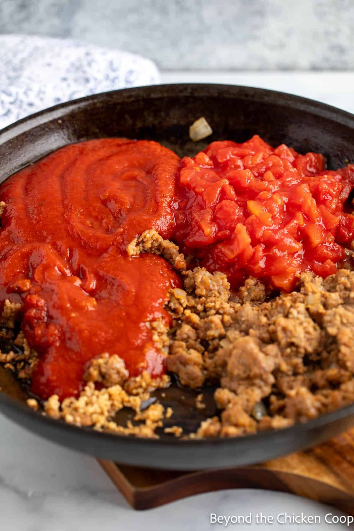 Mariana and diced tomatoes added to sausage in a pan. 