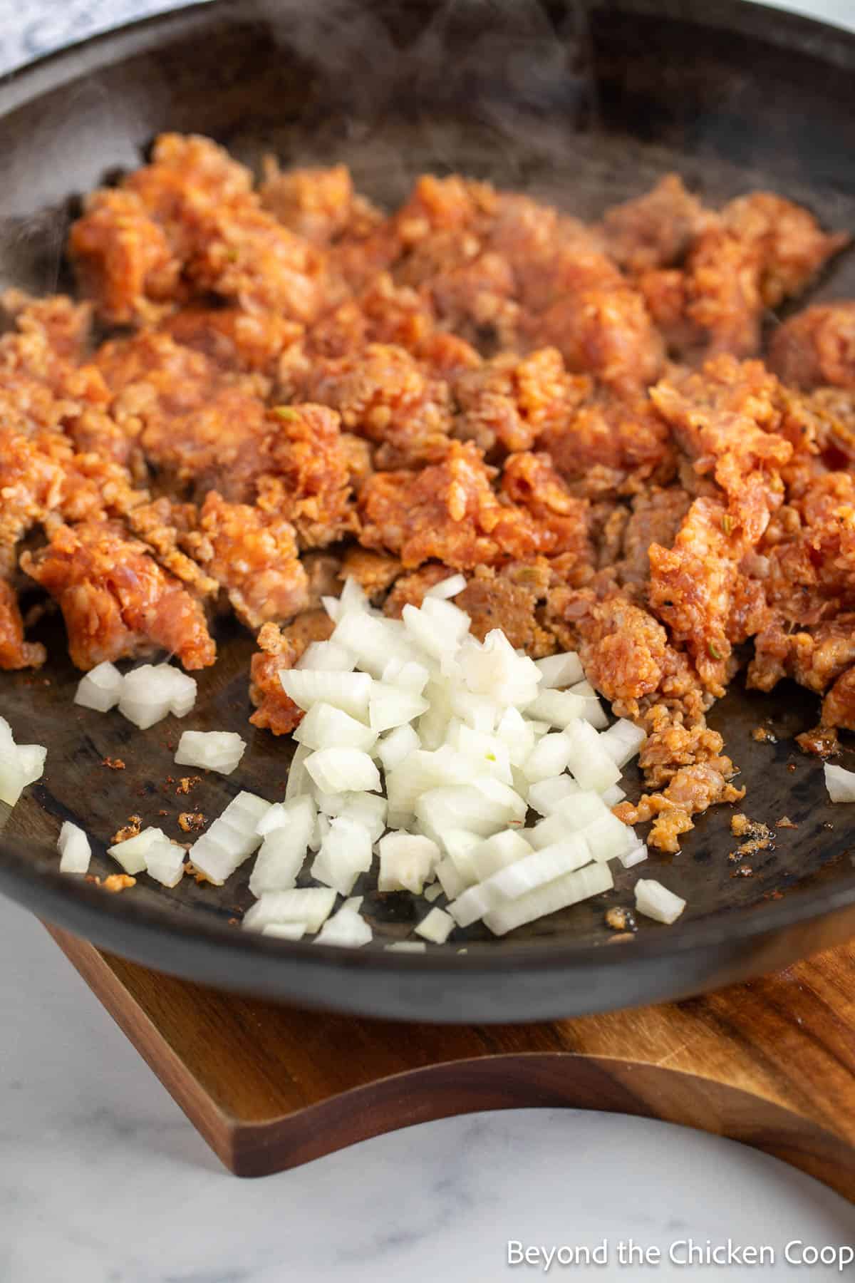 Browned Italian sausage with diced onions in a pan.