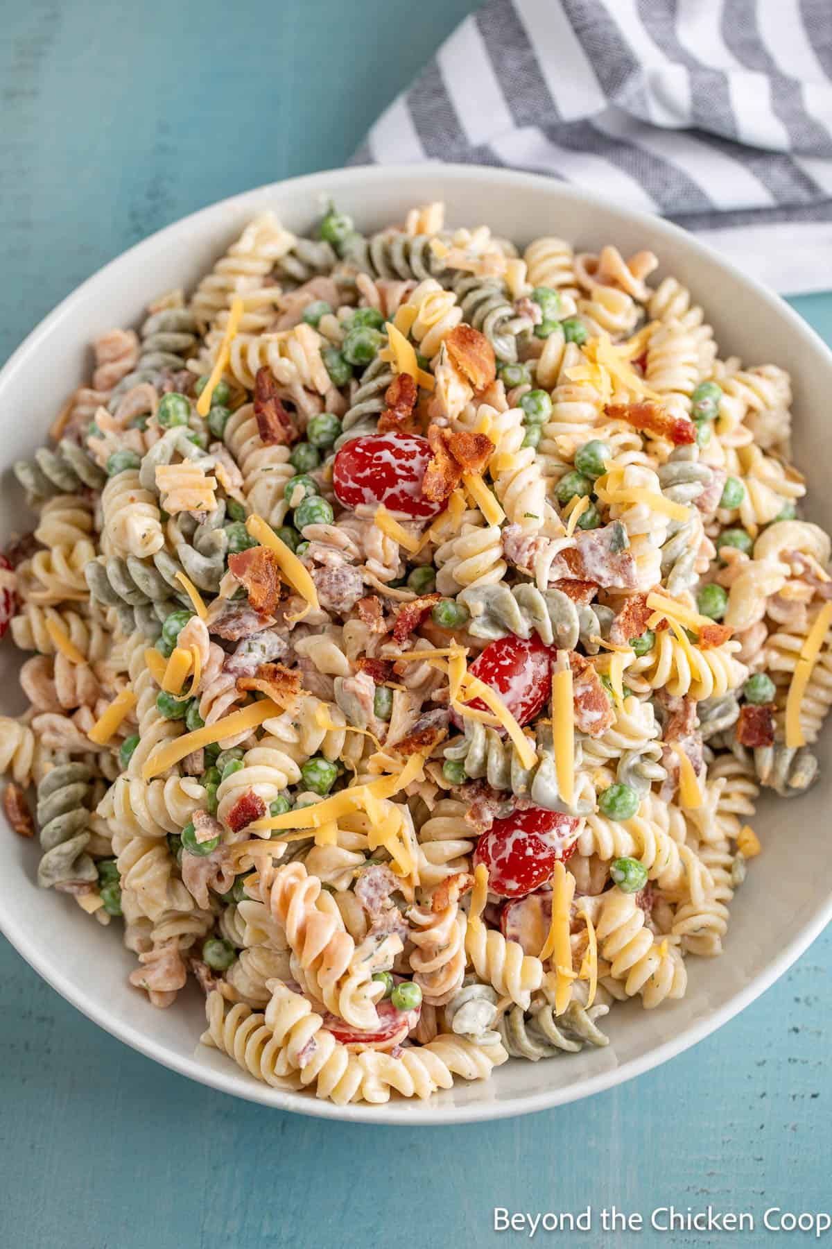 Pasta salad with tomatoes and bacon in a large white bowl. 