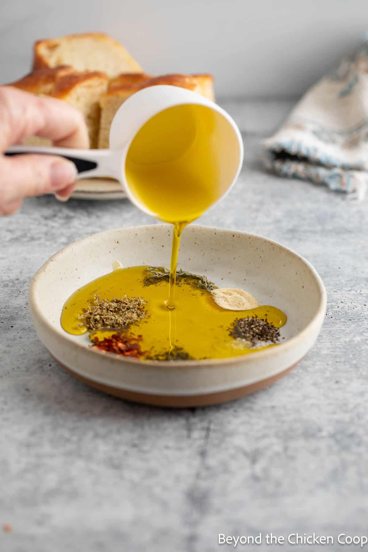 Pouring olive oil into a small bowl with seasonings. 