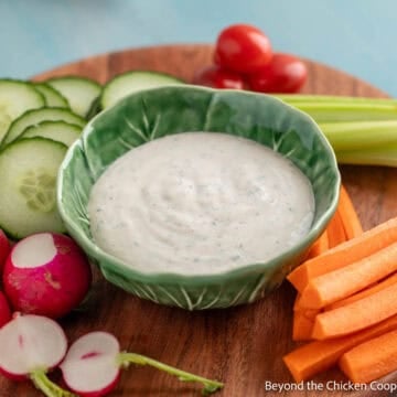 A small green bowl filled with Buttermilk Ranch Dressing surrounded by fresh veggies.