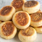 Homemade English Muffins stacked on a white plate.