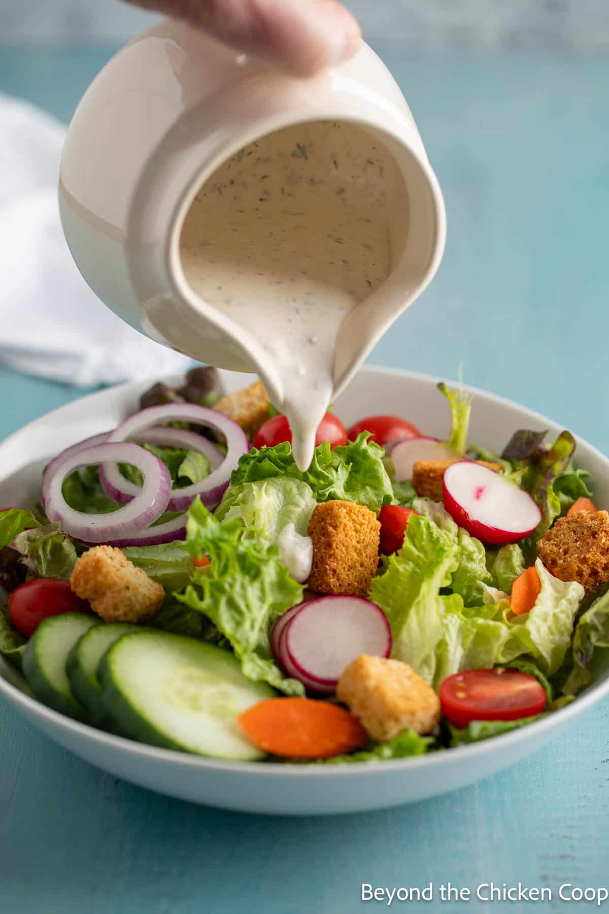 Pouring ranch dressing over a green salad with vegetables. 