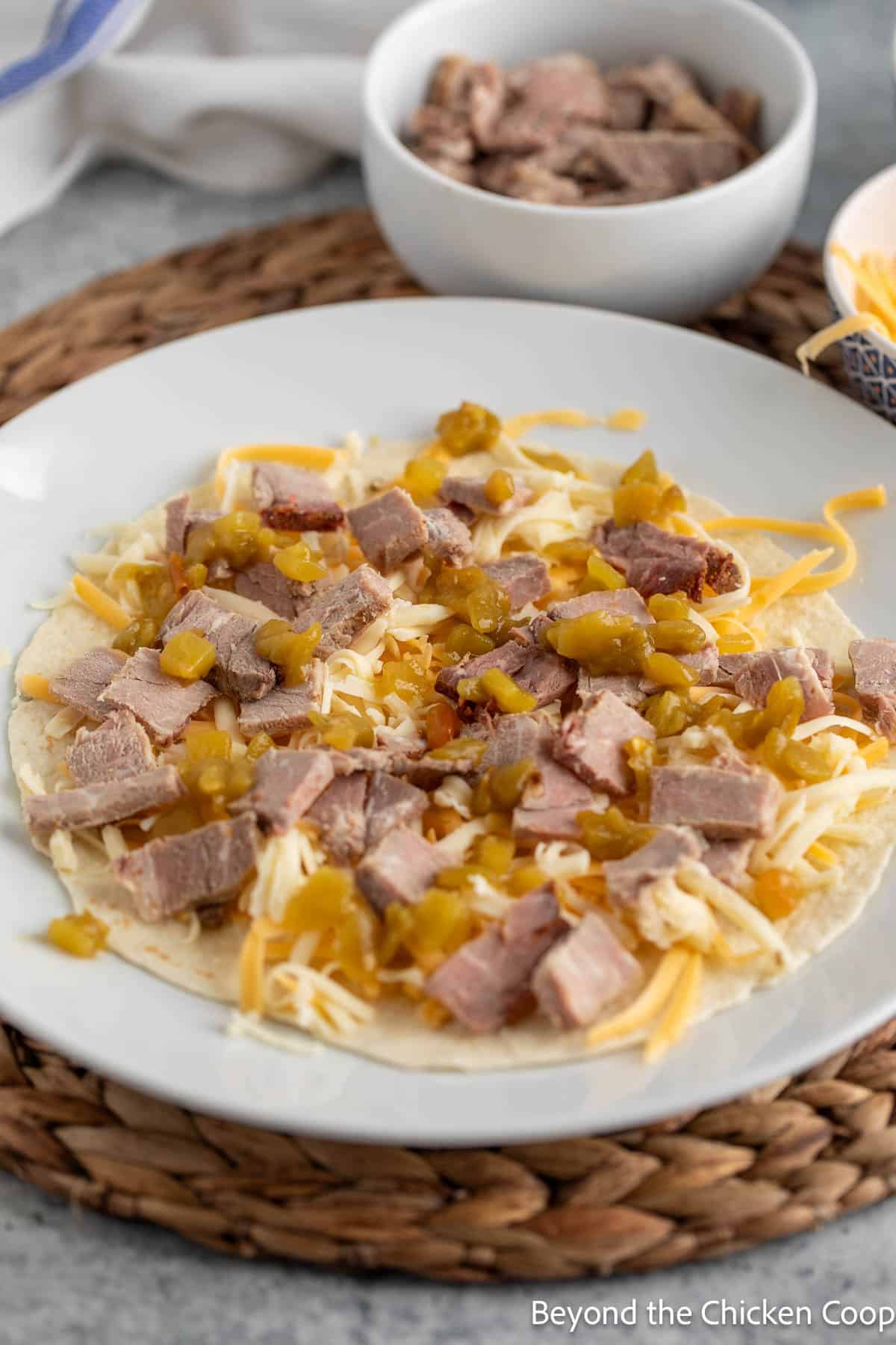 A tortilla topped with shredded cheese and chopped steak. 