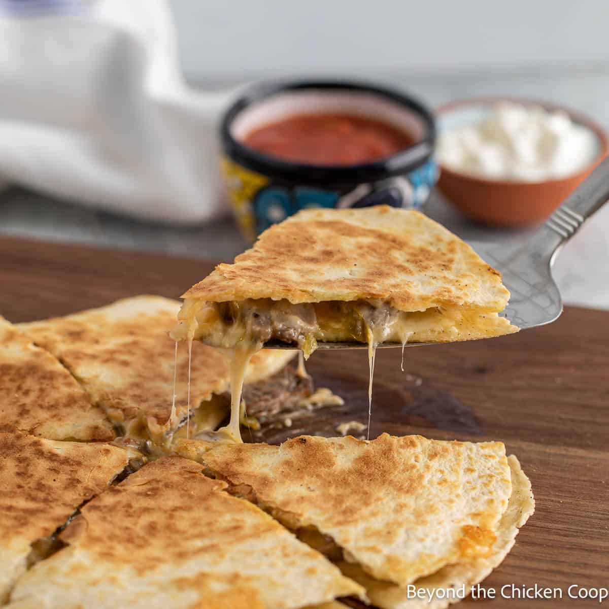 Lifting a slice of quesadilla with melty cheese dripping down from the slice. 