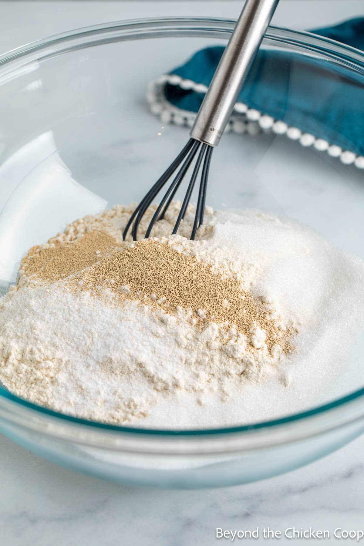 A glass bowl with flour, sugar, and yeast. 