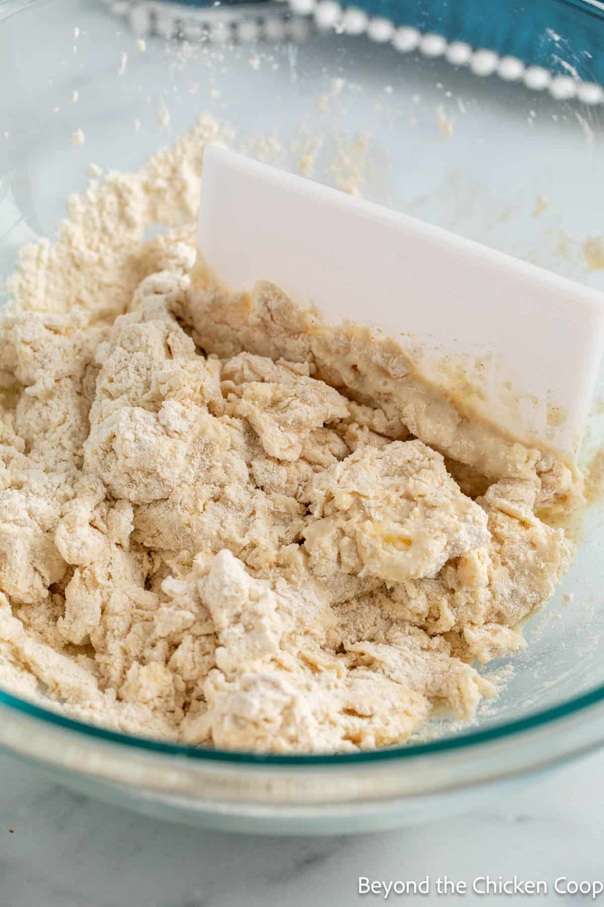 Mixing croissant dough with a soft bench scraper in a glass bowl. 