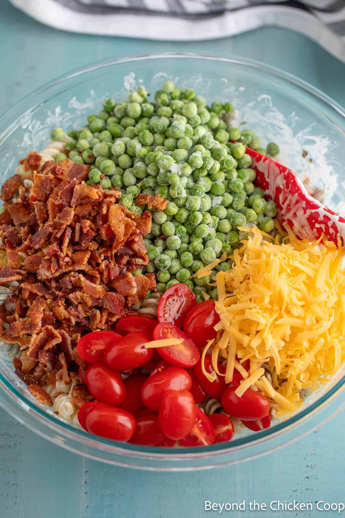 A large bowl filled with pasta, cherry tomatoes, bacon, peas, and cheese.