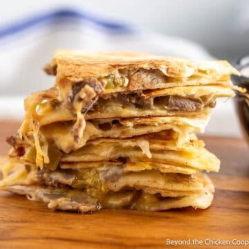 A steak quesadilla cut into wedges and stacked on a wooden board.