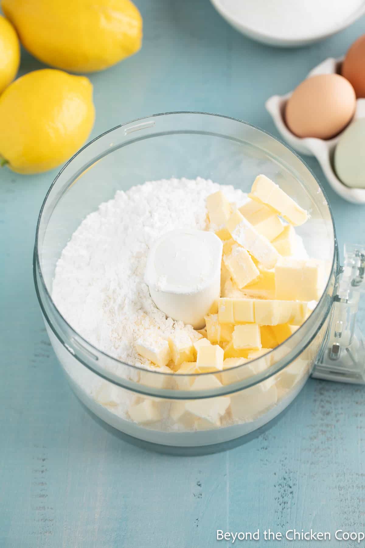 A food processor bowl filled with flour, sugar and butter. 