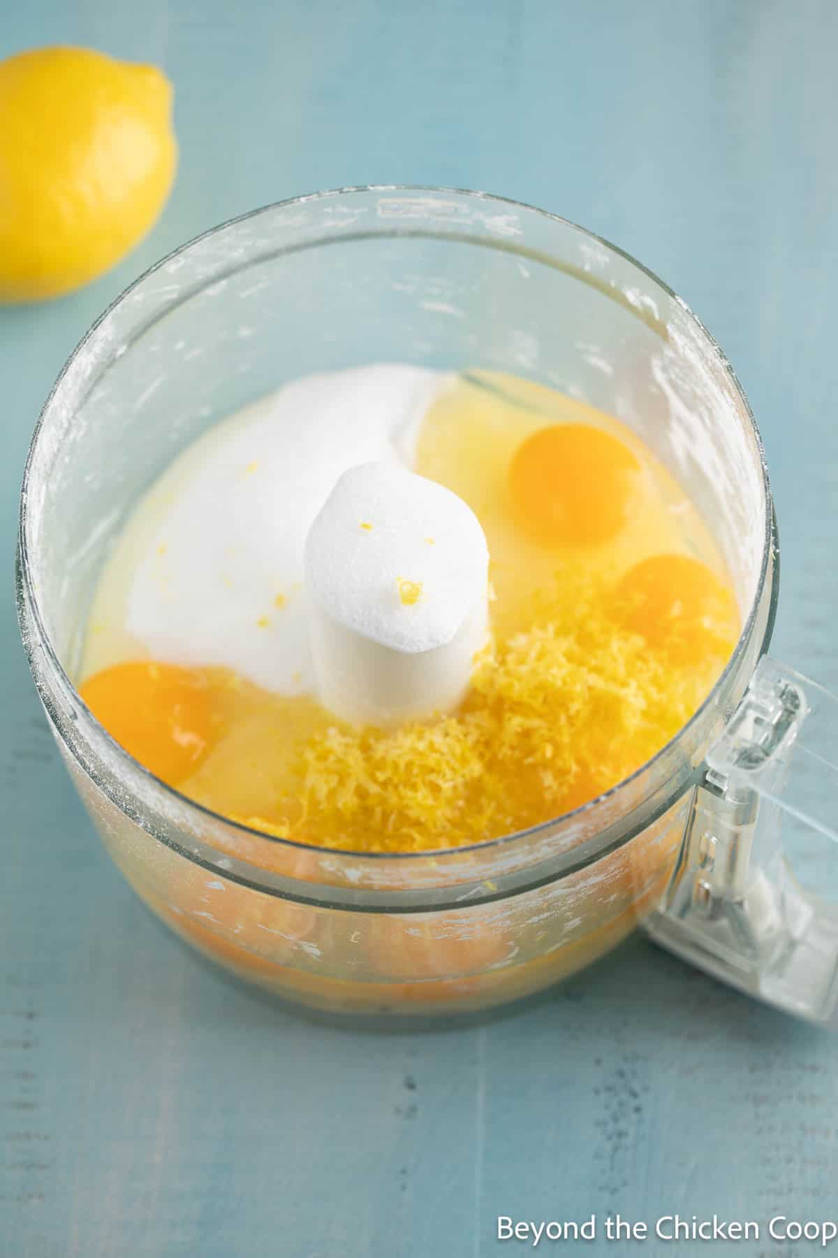 Eggs, sugar, and lemon zest in a food processor bowl. 