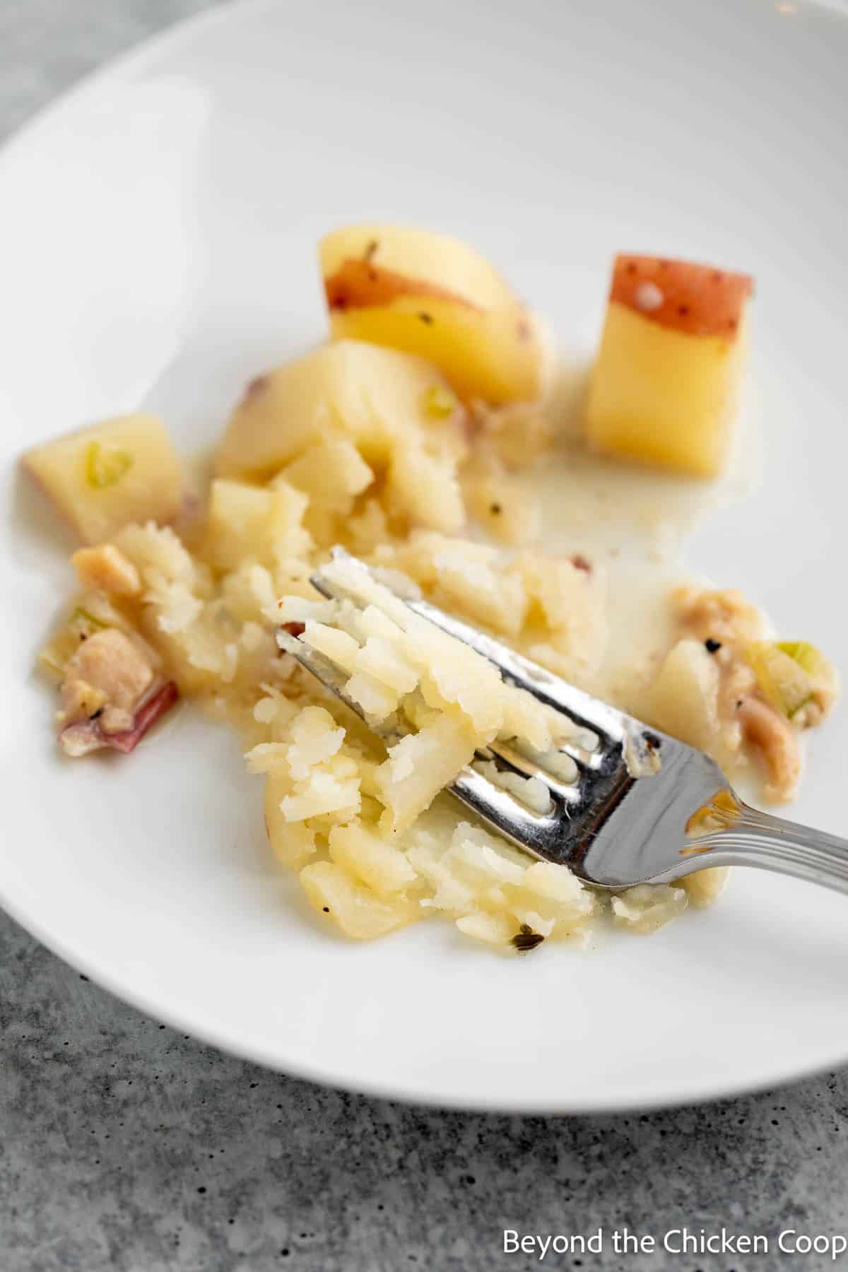 Mashing potatoes with a fork on a plate.