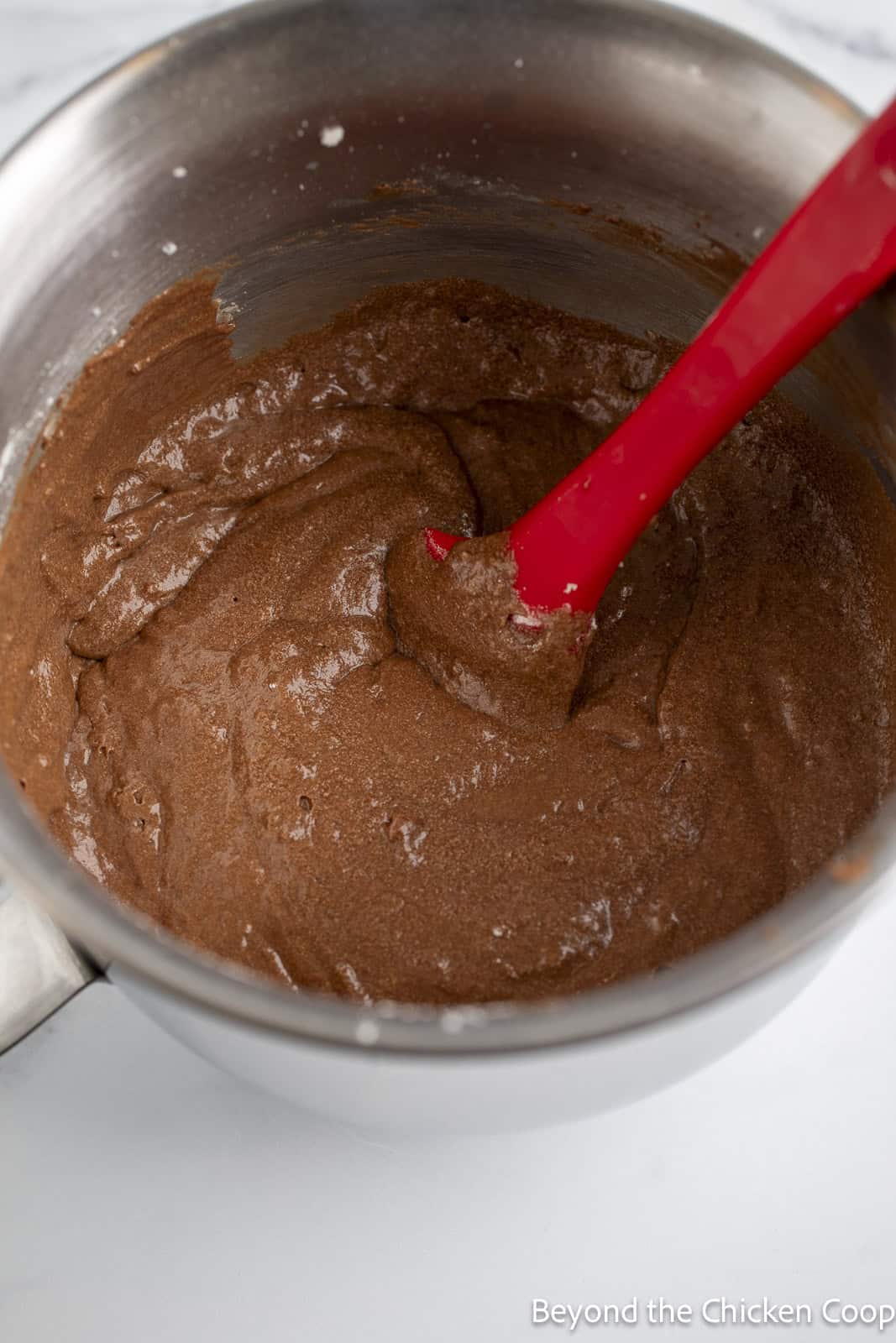 Stirring chocolate cake batter with a red spatula. 