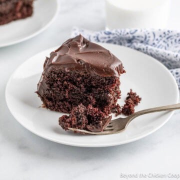 A slice of chocolate layer cake with the end piece sliced off with a fork.