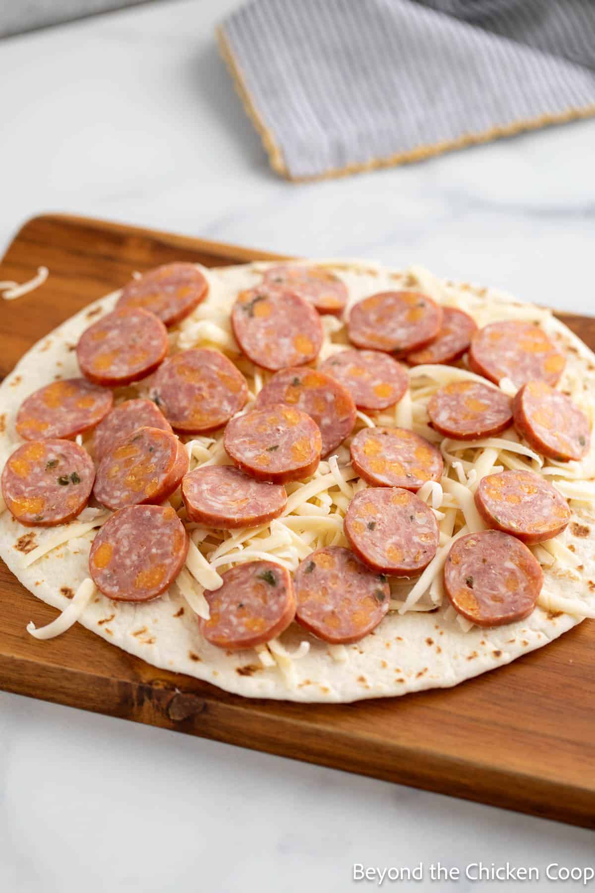 A tortilla topped with smoked sausage slices and shredded cheese. 