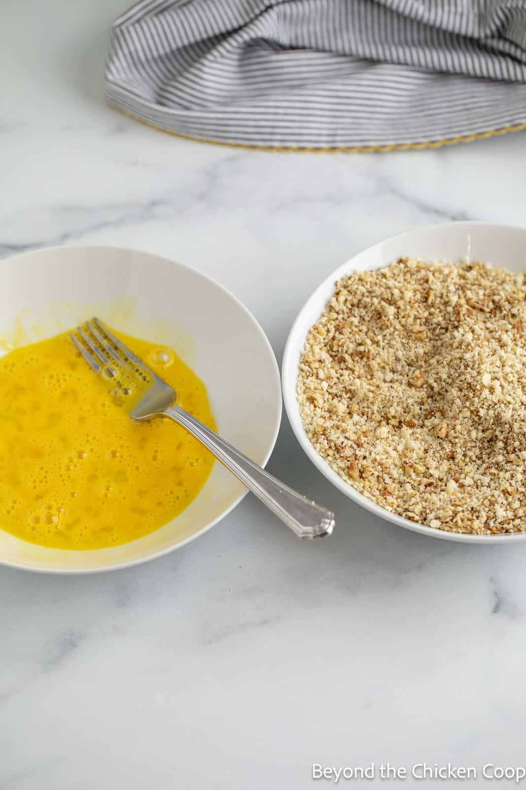 Two bowls filled with a beaten egg and crushed pecans.