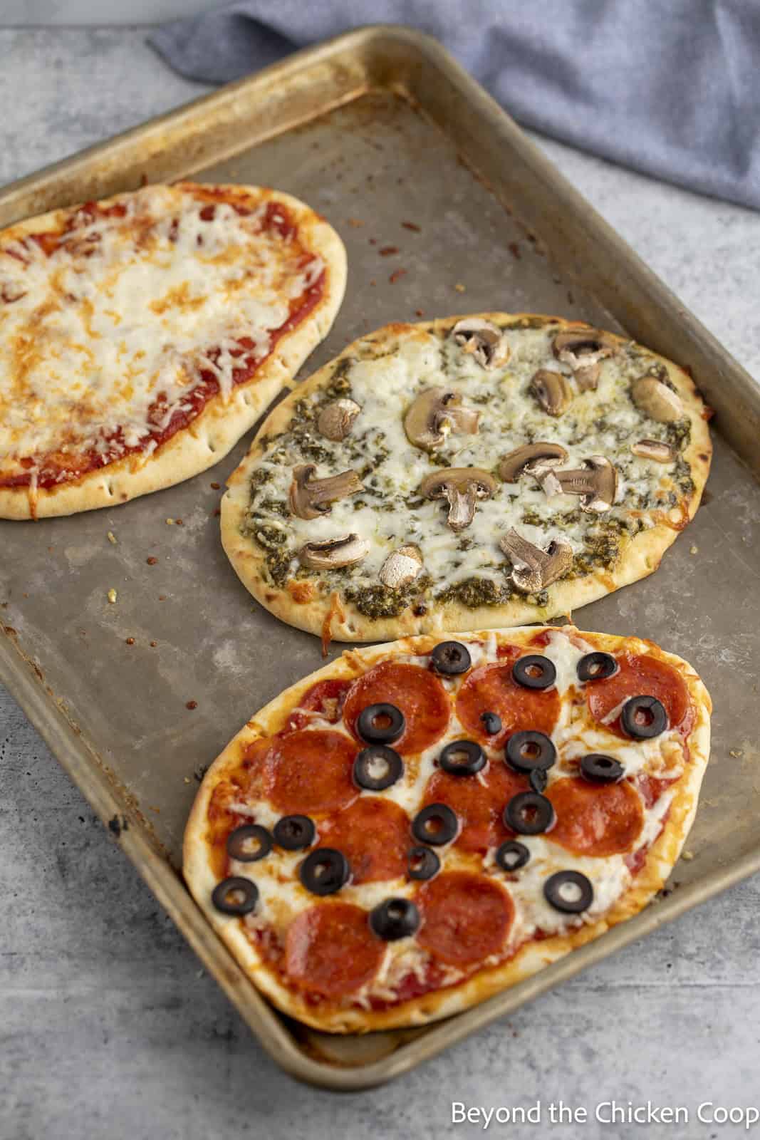 Three small pizzas on a baking sheet. 