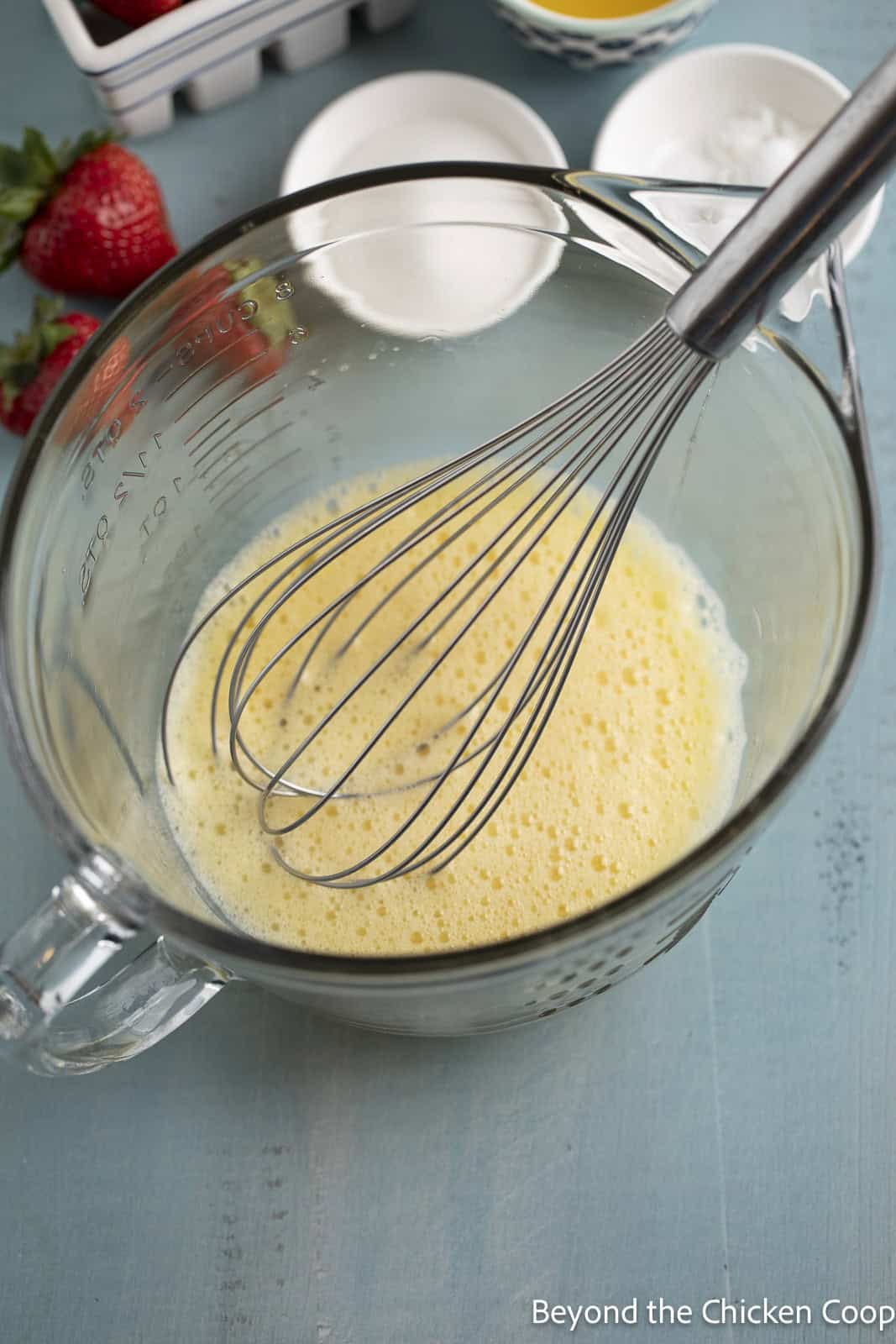 Whipped eggs in a glass bowl with a whisk. 
