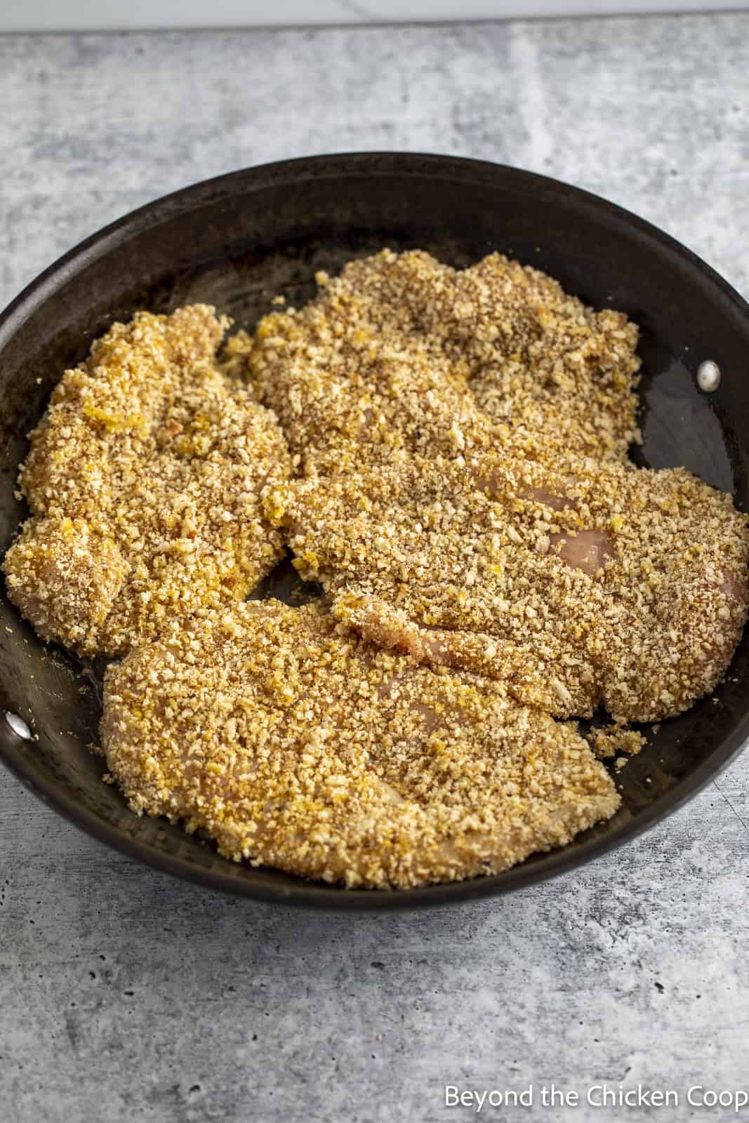 Breaded chicken breasts in a large pan.