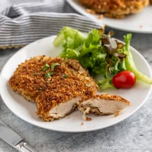 Pecan Crusted Chicken breast on a white plate with a salad.