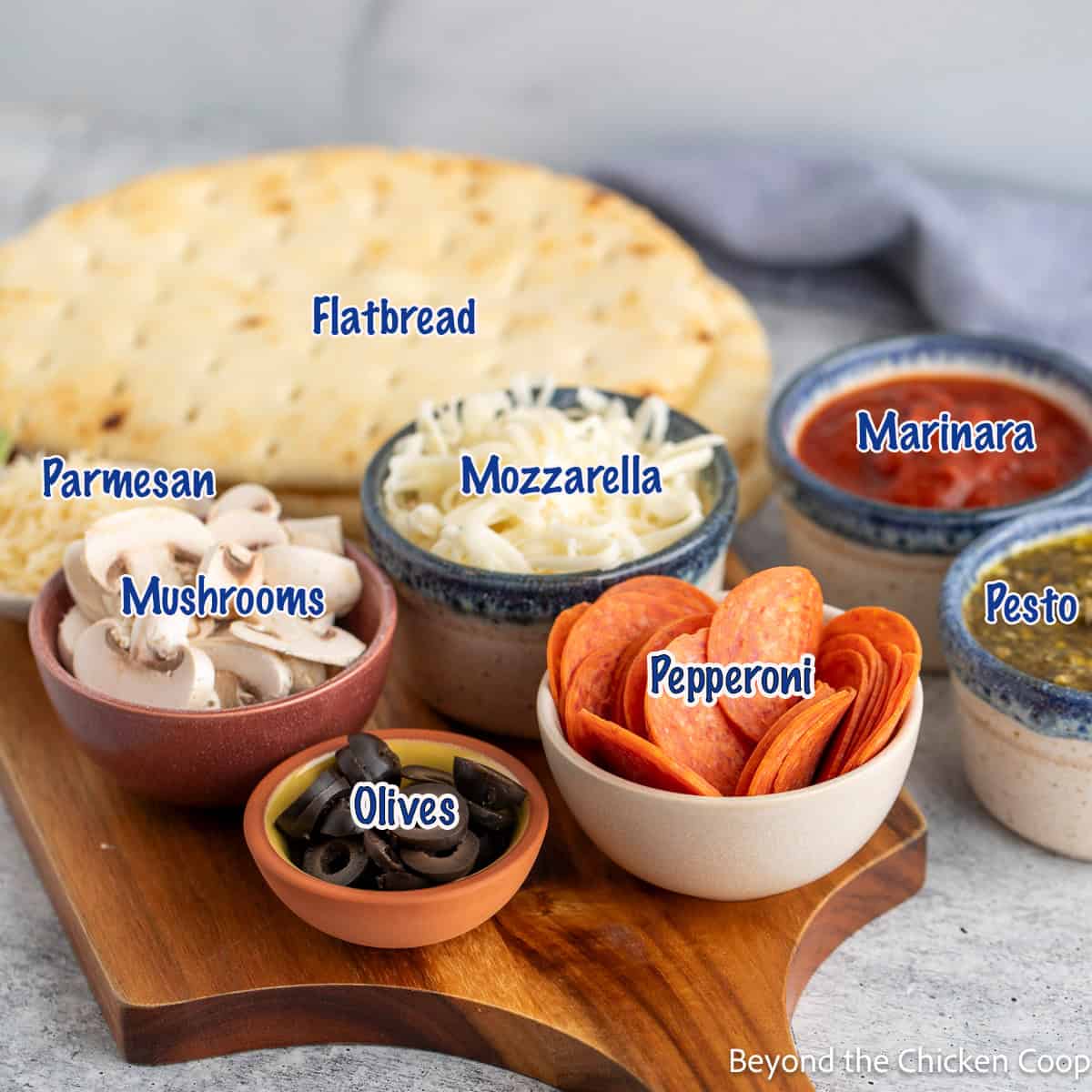 Naan bread next to small bowls filled with pizza toppings. 