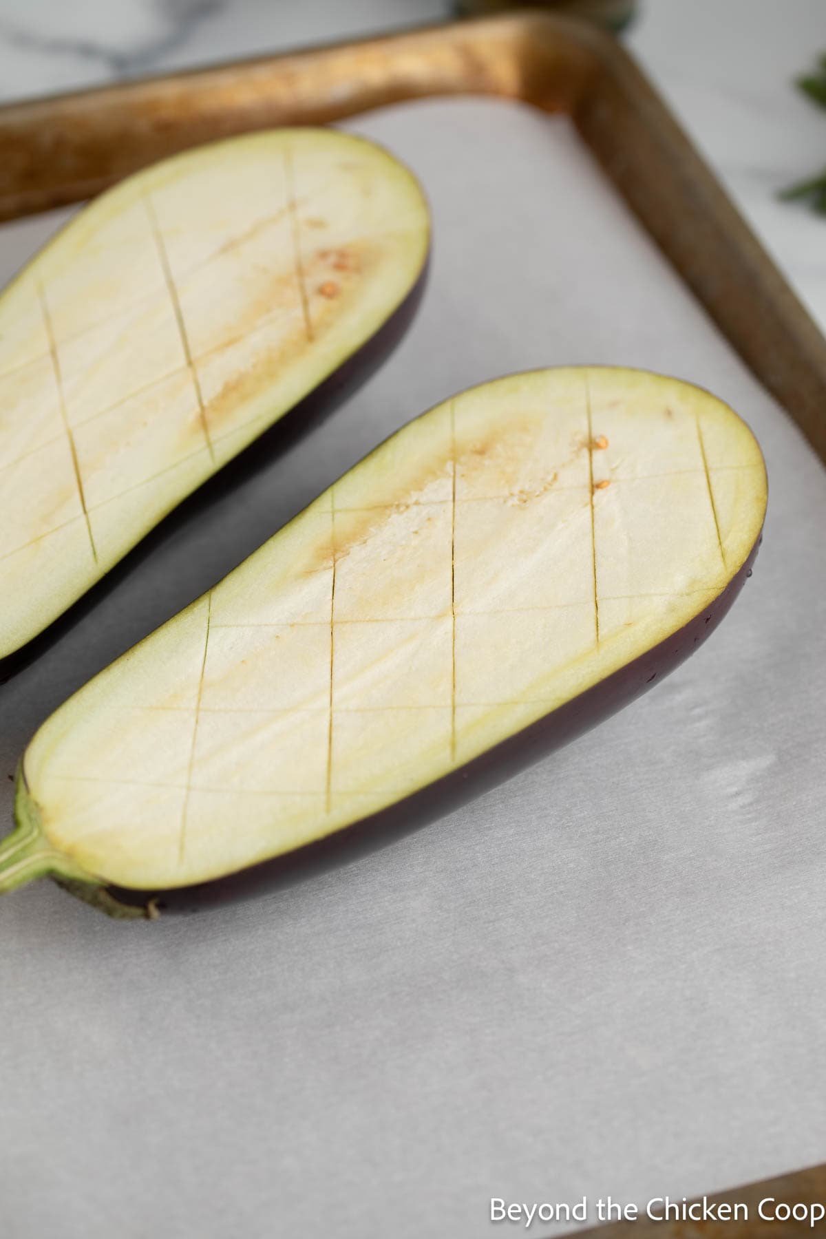 Halved and scored eggplant on a baking sheet. 