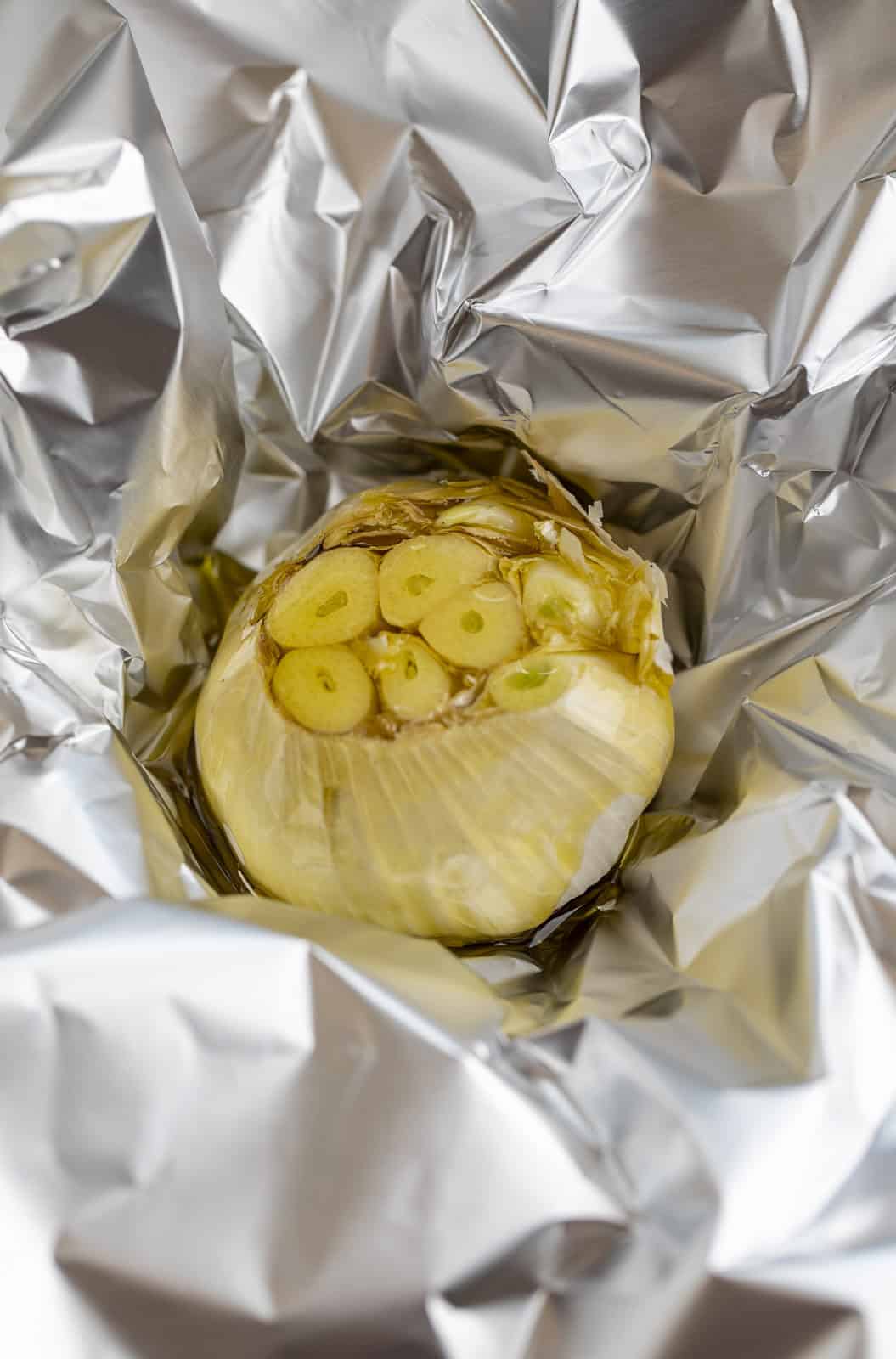 Head of garlic covered with olive oil on a piece of foil.