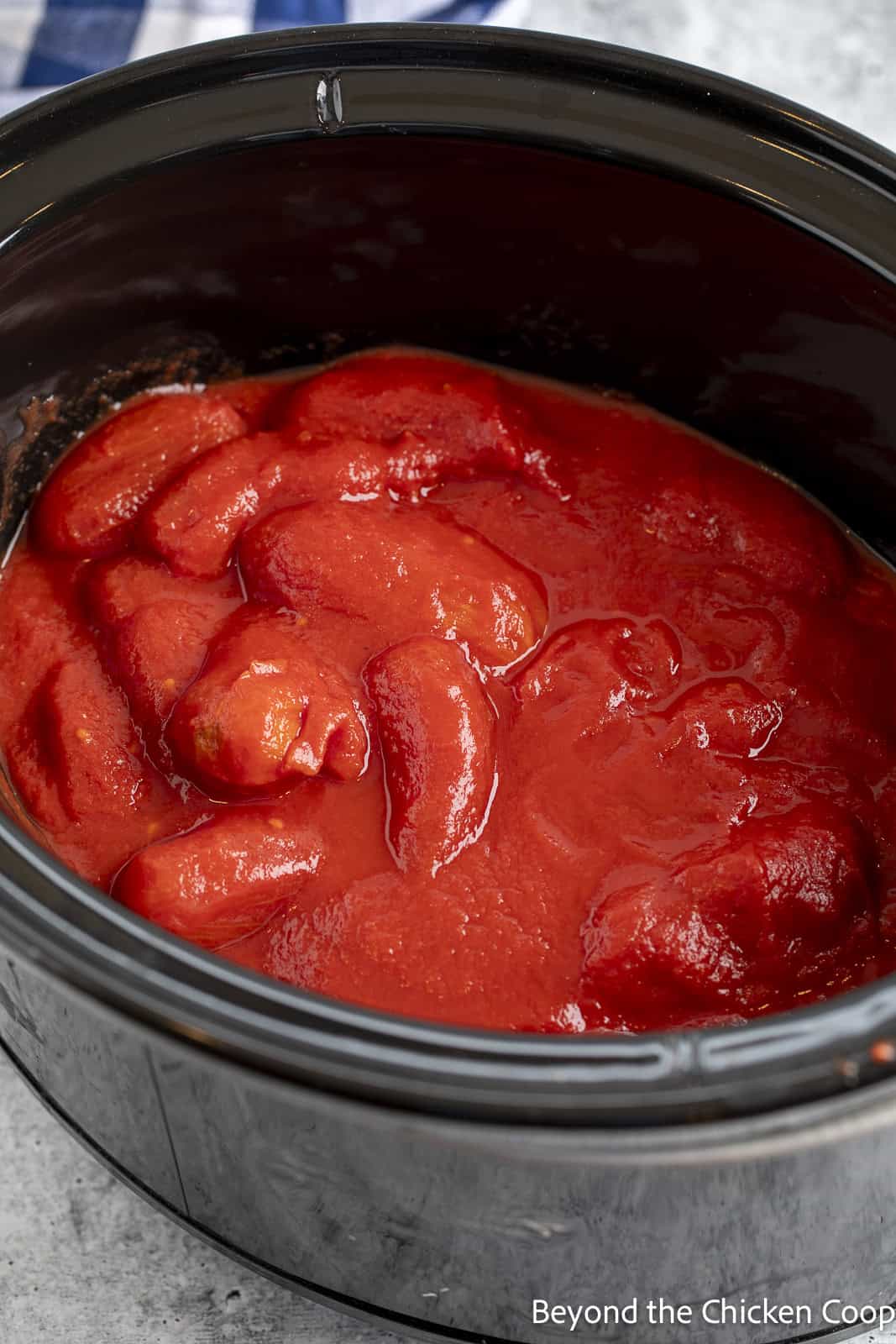 Canned tomatoes added to a crock pot. 