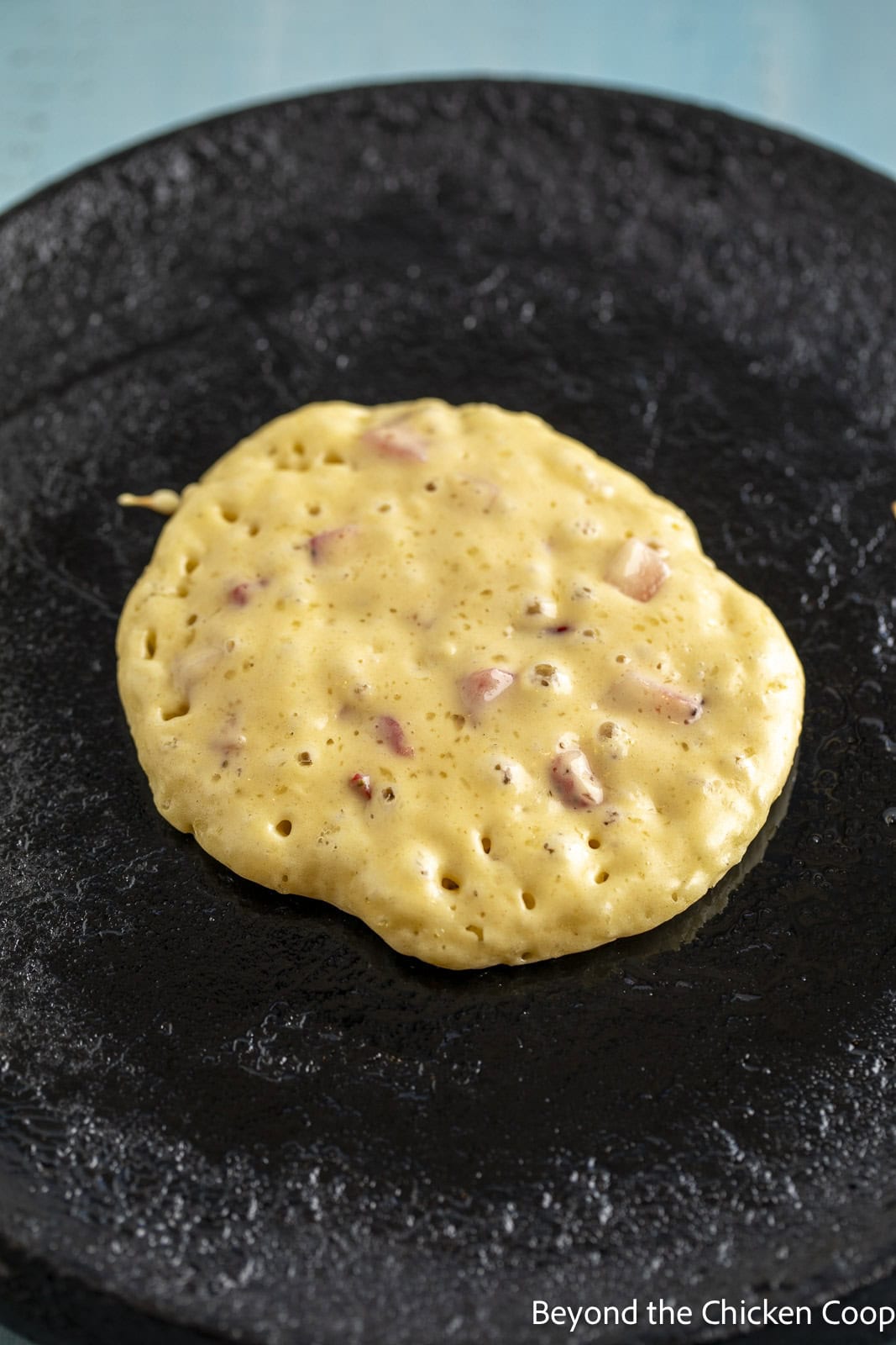 A pancake cooking on a cast iron griddle. 