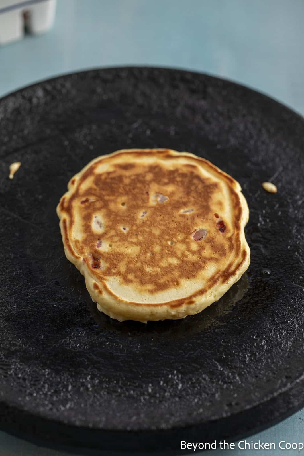 A strawberry pancake cooking on a griddle. 
