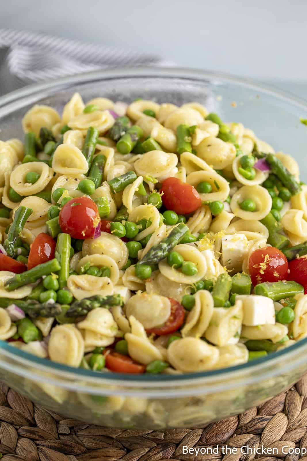 A pasta salad with tomatoes and asparagus in a glass bowl. 