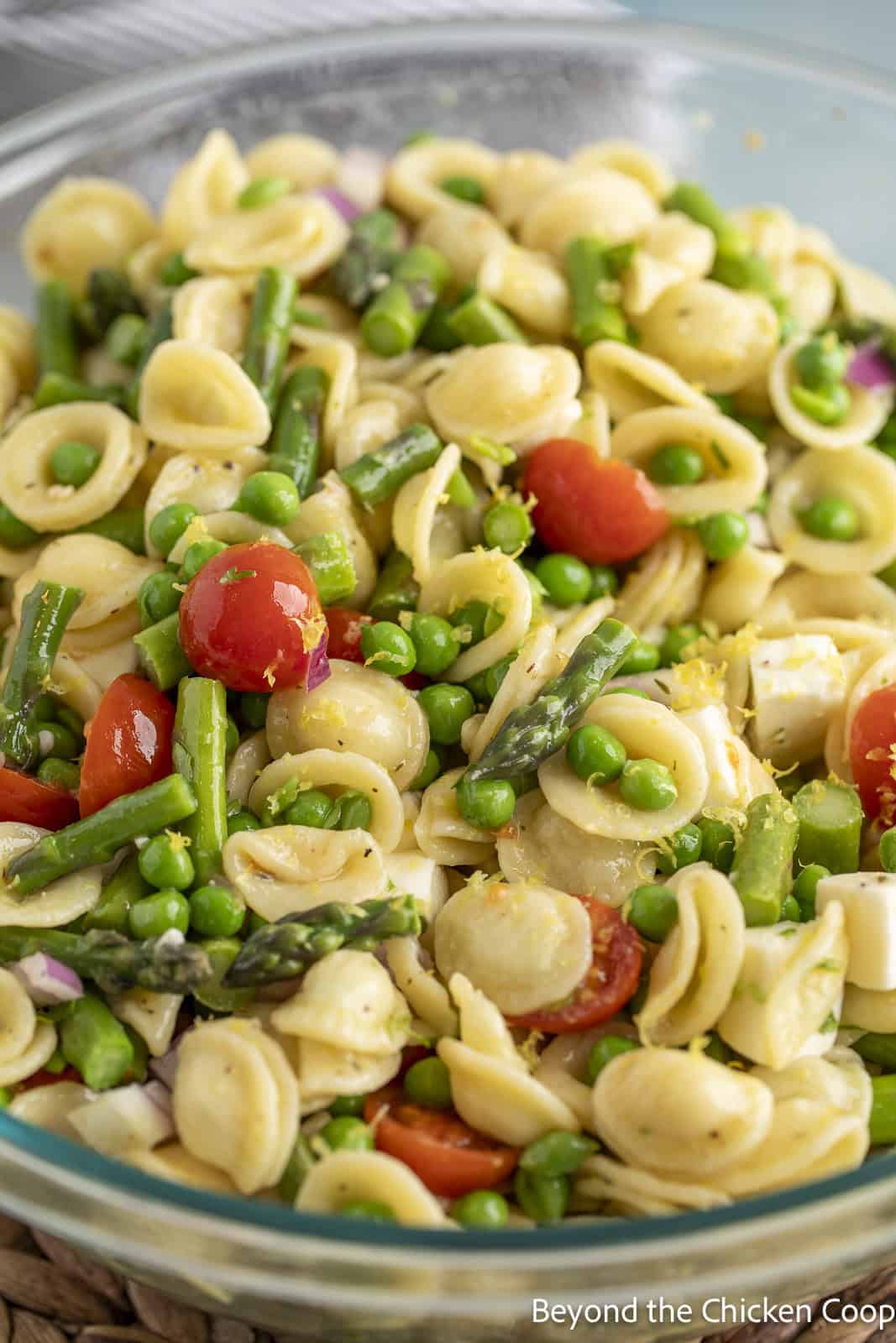 A large bowl filled with orecchiette pasta, cherry tomatoes, peas, and asparagus. 
